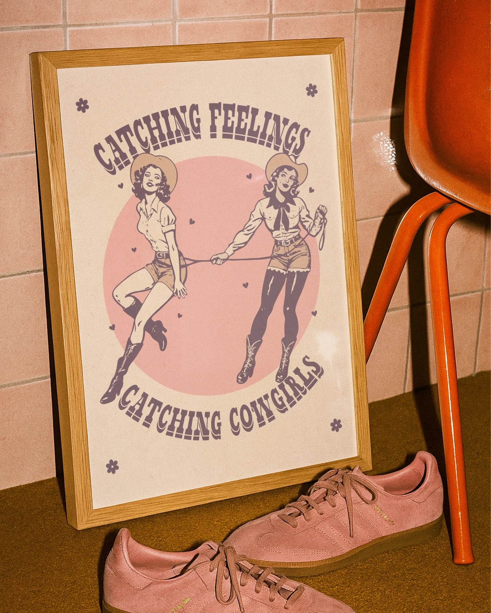 The poster features two illustrated, dreamy retro-style cowgirls capturing each other with a lasso, alongside the text: “Catching Feelings Catching Cowgirls.”