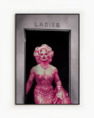 A poster with a muscular drag queen in a sparkling dress, full makeup, and wig, confidently strutting out of the ladies’ room.