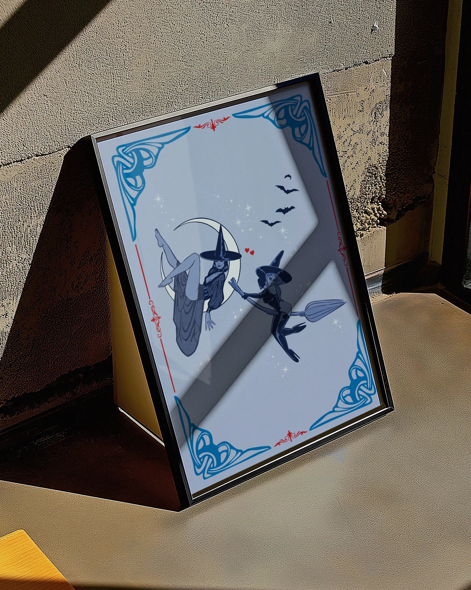 A poster featuring two lesbian witches—one flying on her broomstick while the other lies on the moon. They share a flirtatious glance, surrounded by stars and bats.