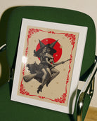 A poster featuring two lesbian witches flying on a broomstick through the night. They share a romantic gaze, surrounded by stars and a large red full moon.