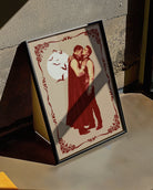 A poster featuring a male vampire kissing another man’s neck, framed by a vintage border, with a full moon and flying bats in the background.