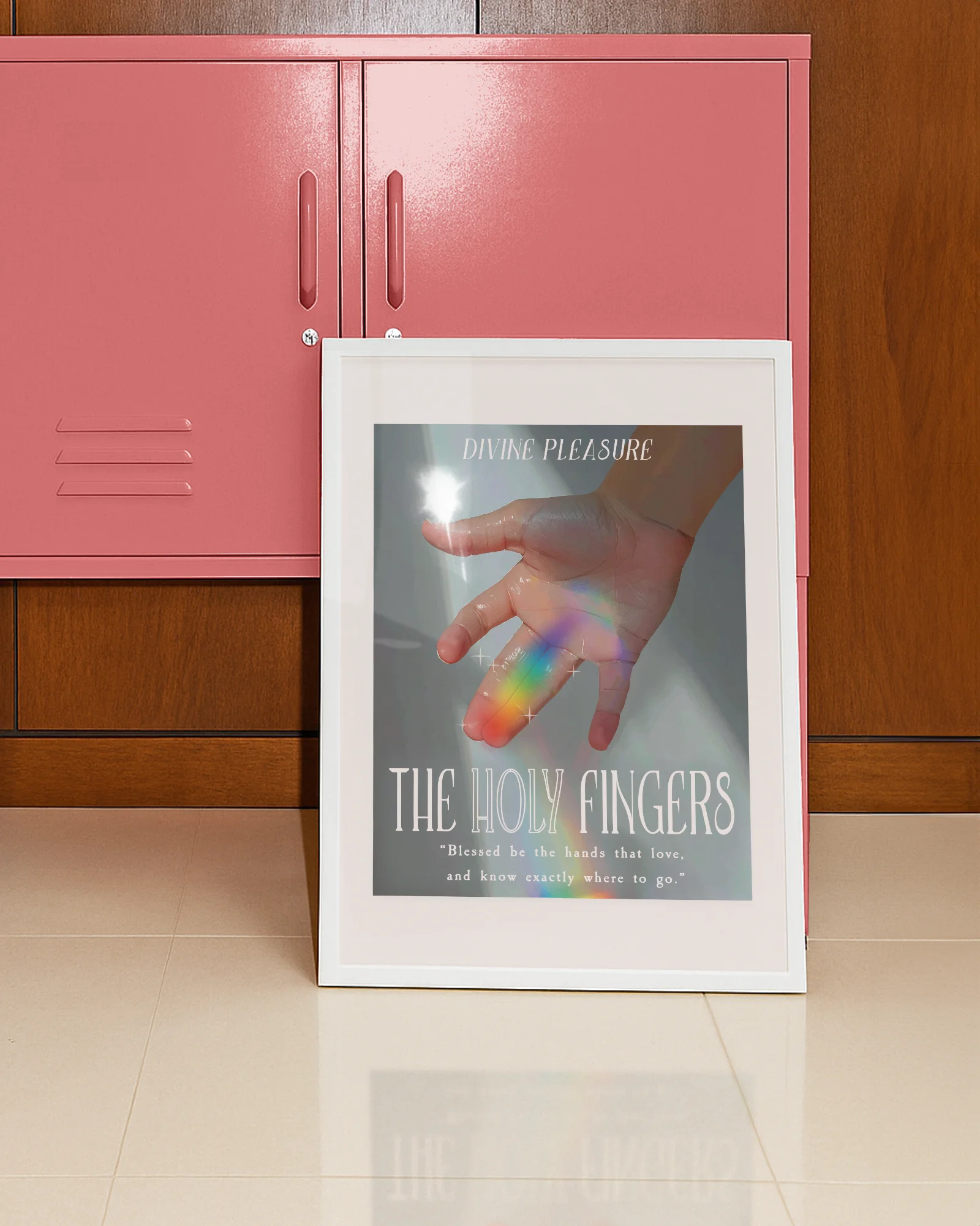 A framed print showing a hand bathed in sunlight, with a ray of rainbow light across the ring and index fingers, with the texts:
“DIVINE PLEASURE – THE HOLY FINGERS” and “Blessed be the hands that love, and know exactly where to go.”