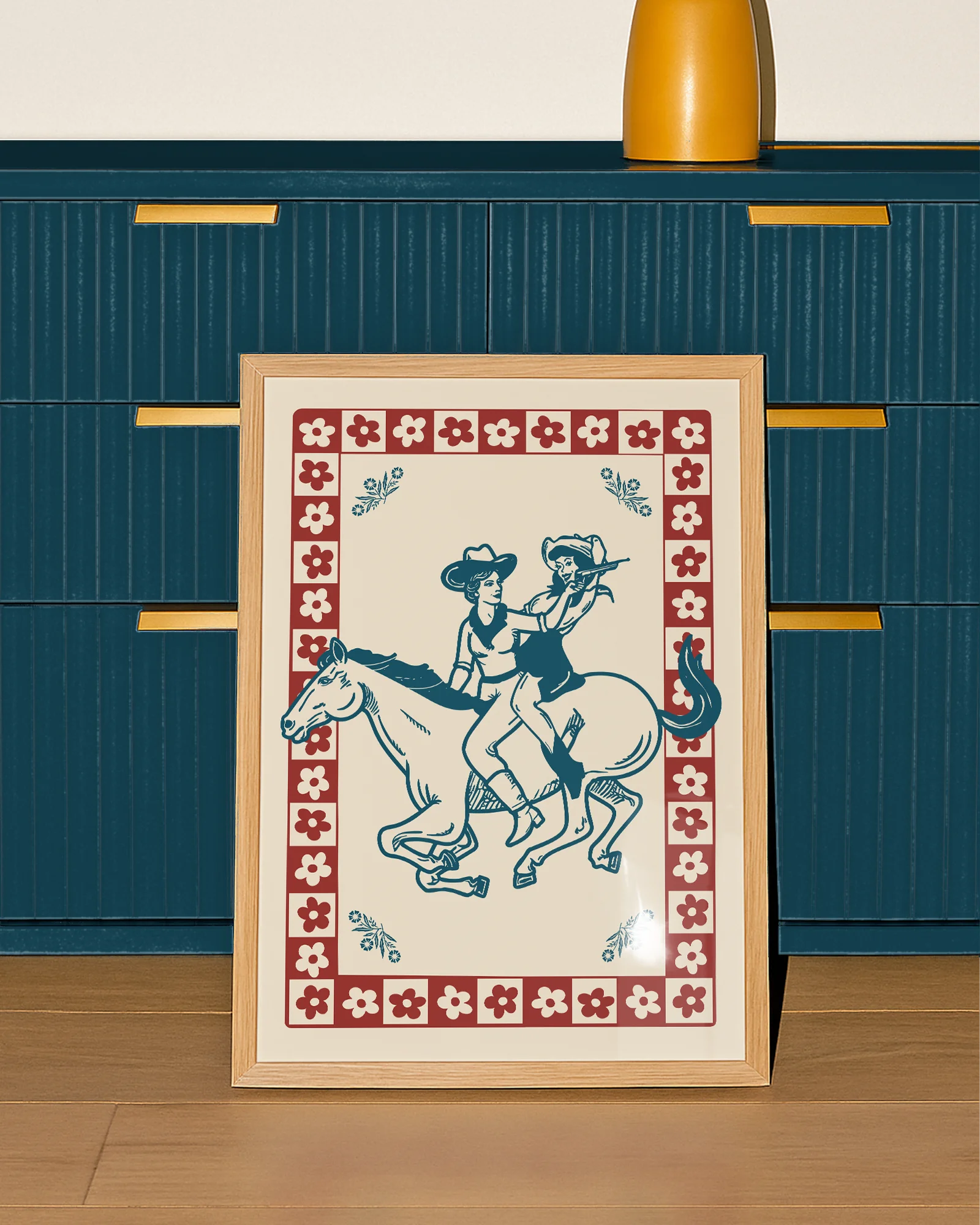 A framed poster featuring two cowgirls riding a horse, surrounded by a retro-style floral frame.