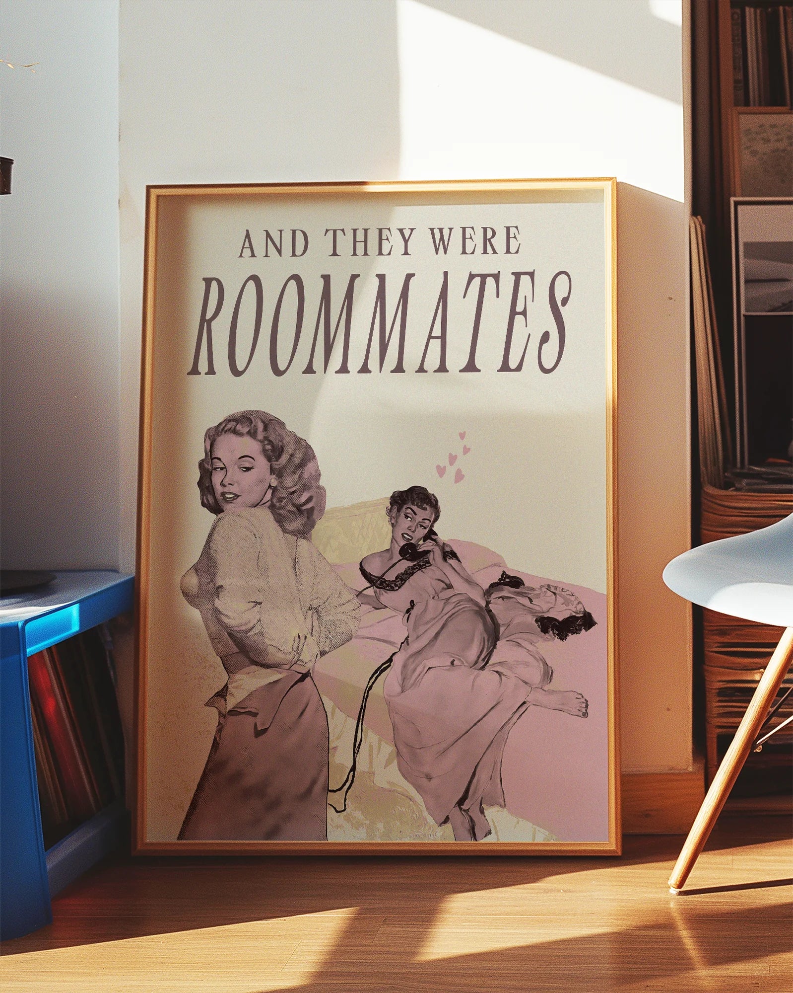 A framed poster depicting a woman lying in bed, and another woman undressing to join her — with the text “AND THEY WERE ROOMMATES.”