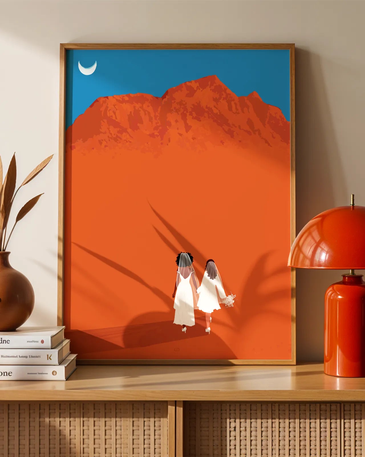 A framed print with a brides couple in white dresses walking hand in hand in a desert.