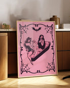 A poster featuring a female devil sitting on the edge of a coffin, while a female vampire sits inside. They hold each other’s hands romantically, creating a mysterious and intimate atmosphere.