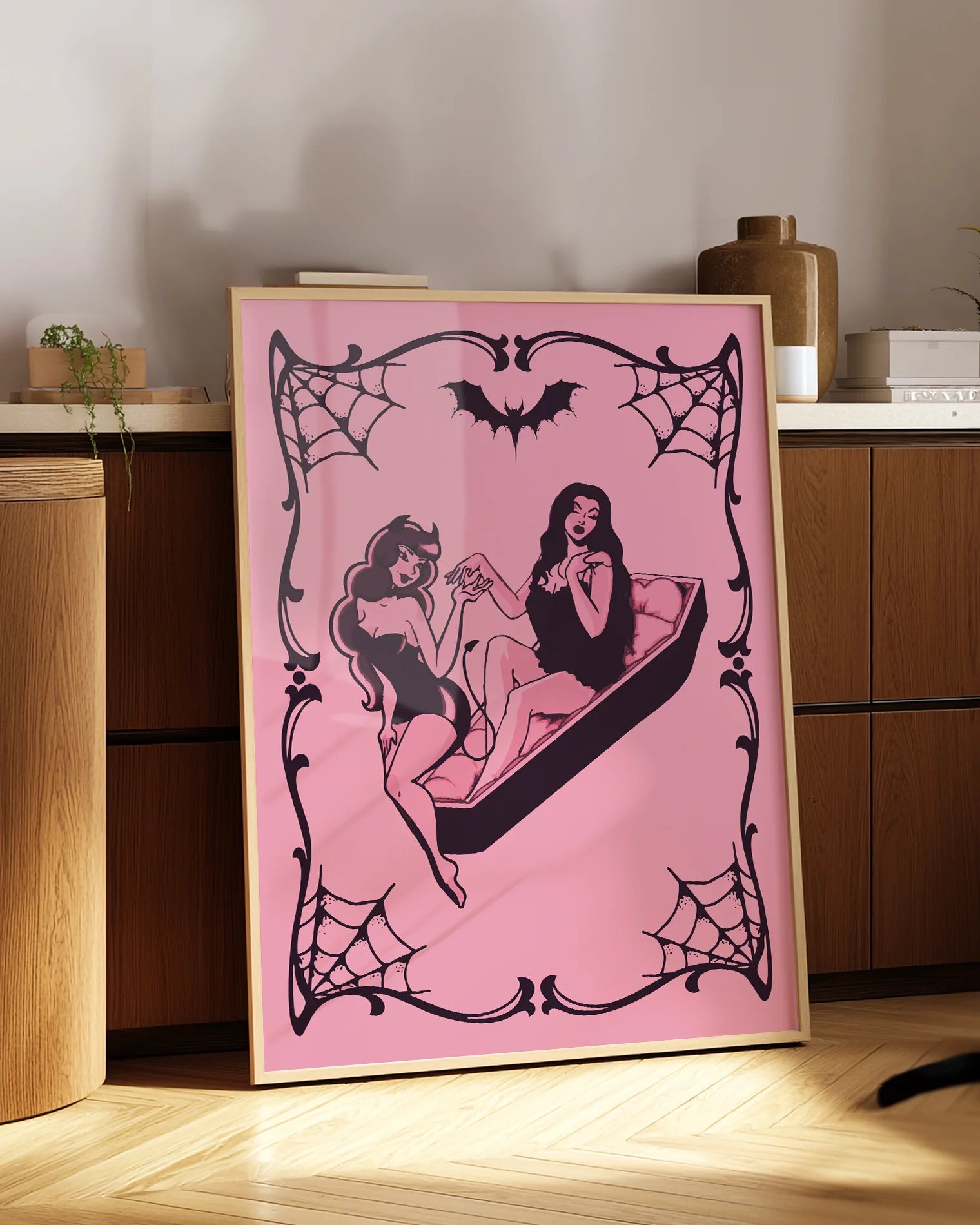 A poster featuring a female devil sitting on the edge of a coffin, while a female vampire sits inside. They hold each other’s hands romantically, creating a mysterious and intimate atmosphere.