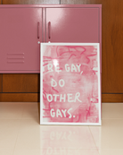 A framed poster with the text 'BE GAY, DO OTHER GAYS.', against a pink, abstract background.
