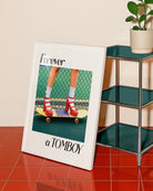 A framed print with a girl in red high heels standing on a skateboard, with the text: 'Forever a TOMBOY'.