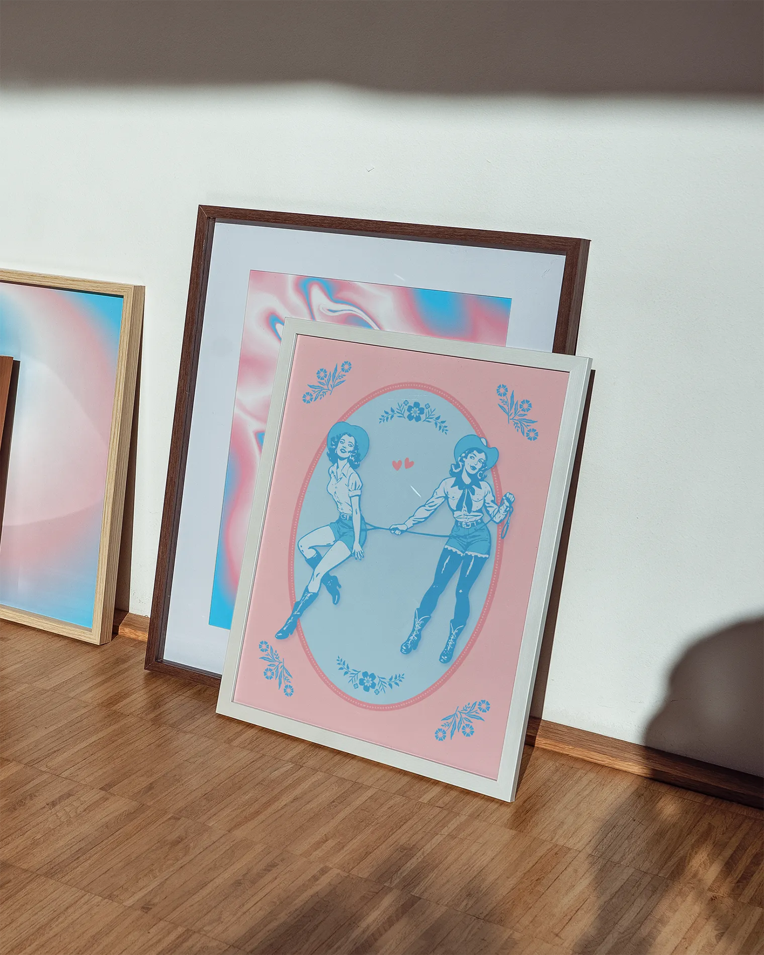 A gallery wall with three sapphic and transgender themed prints.