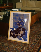 A framed poster with two, older men kissing on a couch.