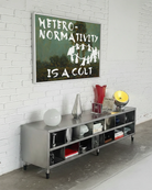 A framed poster depicting a group of people dancing in a cult-like circle, accompanied by the text “Heteronormativity Is a Cult.”