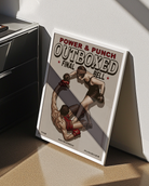 A framed poster featuring a female boxer completely dominating the ring, knocking down her male opponent, with the texts: “POWER & PUNCH”, “OUTBOXED”, “FINAL”, and “THE PATRIARCH PUNISHER.”