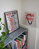 A framed print featuring the text “PROTECT THE DOLLS MEANS:” followed by:
employ the dolls
connect the dolls
uplift the dolls
support the dolls
befriend the dolls
house the dolls
feed the dolls
celebrate the dolls
showing up for the dolls