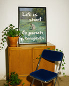 En postern som föreställer en kvinna som plockar blommor i ett öppet fält, i en klassisk oljemålnings-stil med texten 'Life is short Go punch a homophobe".