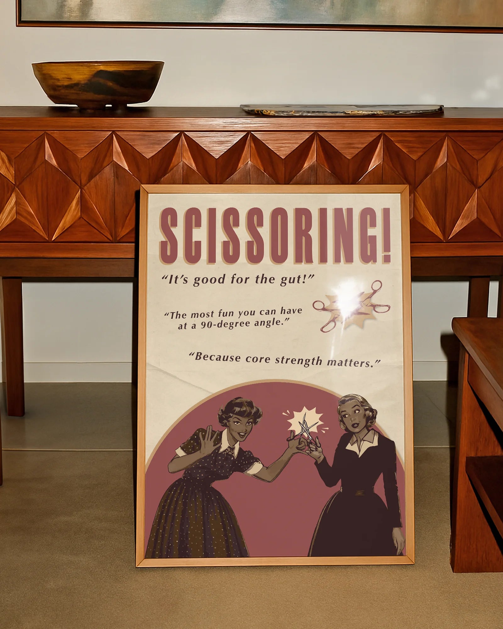 A print featuring two women playfully holding a pair of scissors toward each other, with the texts: “SCISSORING!”, “It’s good for the gut!”, “The most fun you can have at a 90-degree angle”, and “Because core strength matters.”