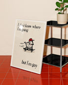 A framed poster with a cute, curly dog on a skateboard with the text 'I don't know where I'm going but I'm gay.