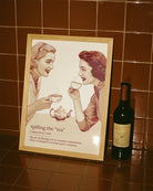 A framed poster featuring two women gossiping over tea, accompanied by the text: “Spilling The Tea – Verb – The act of sharing new or sensitive information, often exchanged in trusted queer company.”